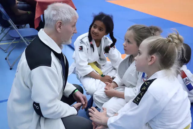 Begeleider spreekt met jonge judoka’s langs de tatami